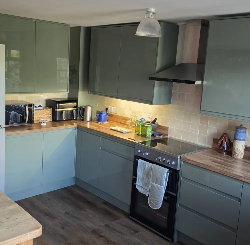 New L-shaped sage green gloss kitchen with wood-effect worktops, under-cabinet lighting and LVT flooring