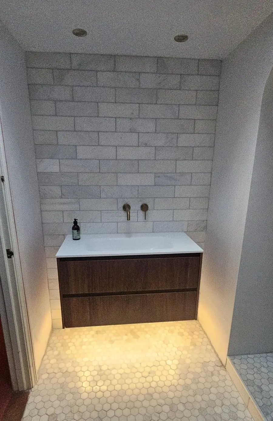 Fluted wall-hung vanity with brass taps over a hexagon marble floor